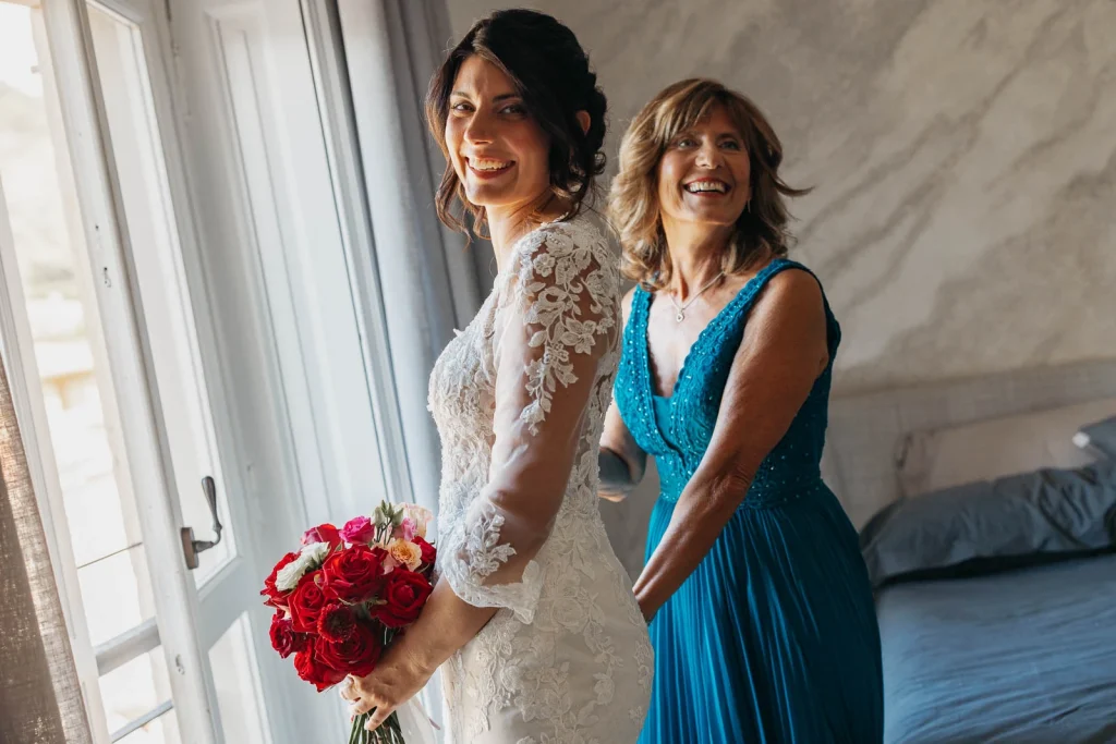 Bride standing between her mother and bridesmaid holding red bouquets