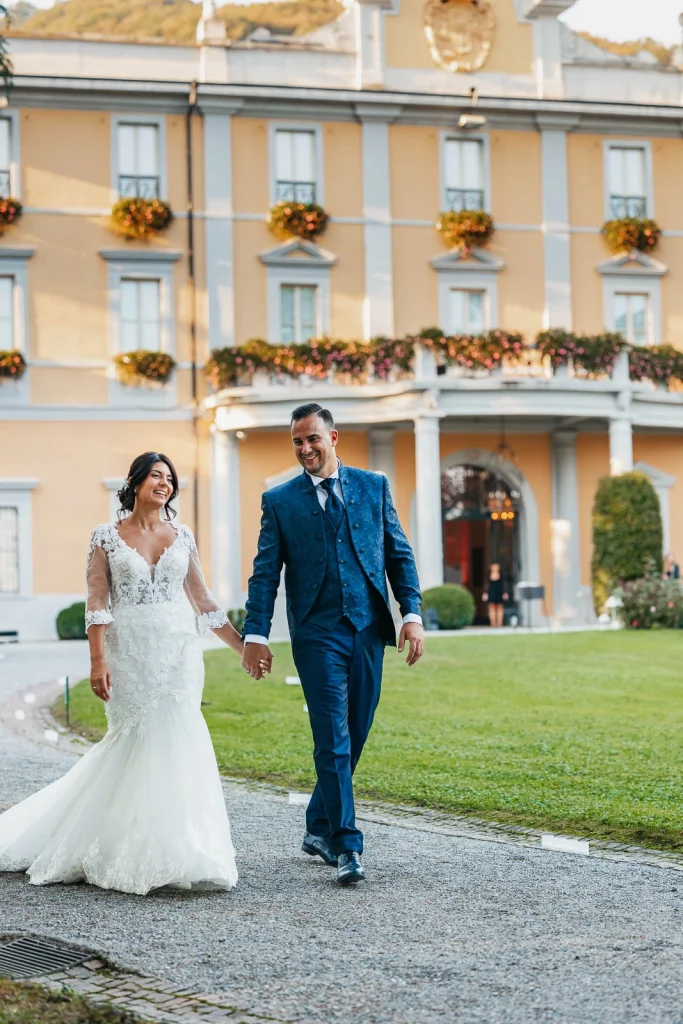 Newlyweds walking hand in hand in front of Villa Acquaroli