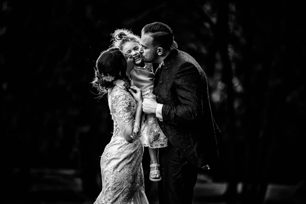 Black and white photo of bride, groom, and daughter hugging