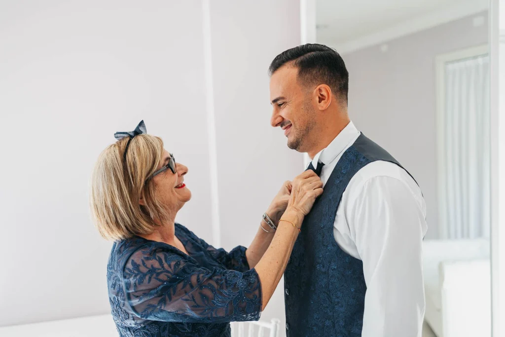 Groom smiling with his mother as she adjusts his boutonniere