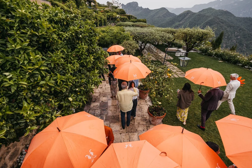 Ravello Wedding at Belmond Hotel Caruso – Amalfi Coast Destination Wedding 61 Guests holding orange umbrellas on the garden path