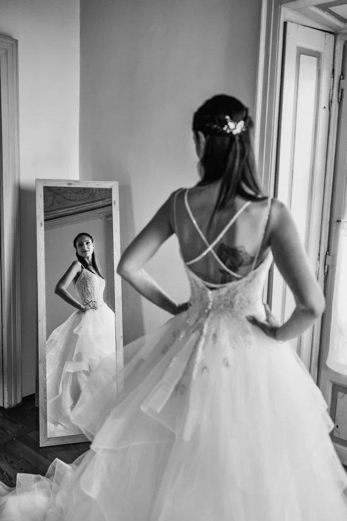 Dream Wedding at Villa Le Due Torrette in Erba: The Elegance of a Lake Como Celebration 24 Bride from behind, standing in front of the mirror in her gown