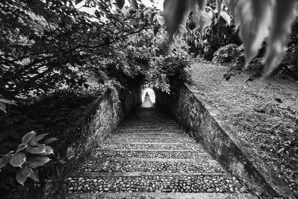 Dream Wedding at Villa Le Due Torrette in Erba: The Elegance of a Lake Como Celebration 34 Black and white photo of bride walking down ancient stone stairs