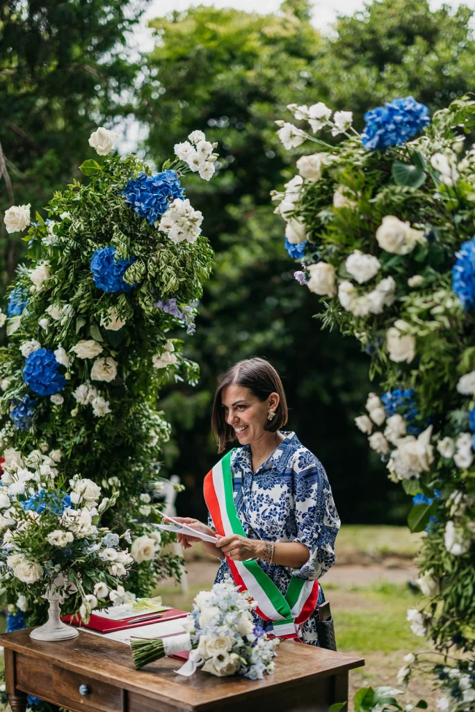Dream Wedding at Villa Le Due Torrette in Erba: The Elegance of a Lake Como Celebration 38 Wedding celebrant reading during the ceremony, surrounded by blue hydrangeas