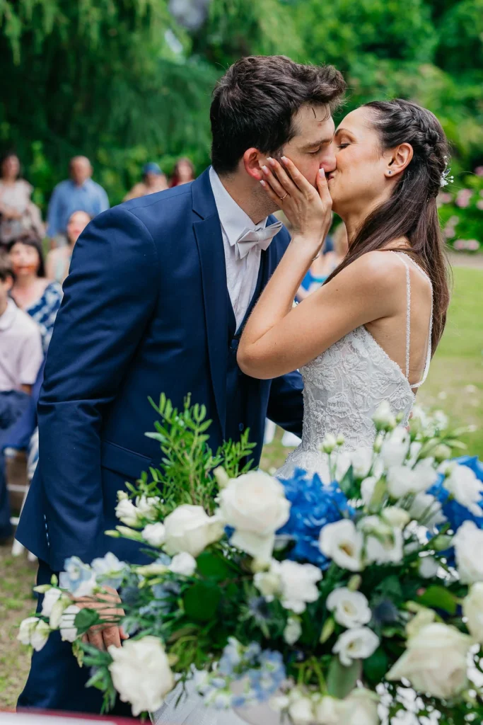 Dream Wedding at Villa Le Due Torrette in Erba: The Elegance of a Lake Como Celebration 46 Groom kissing bride near blue floral arch at Villa Le Due Torrette