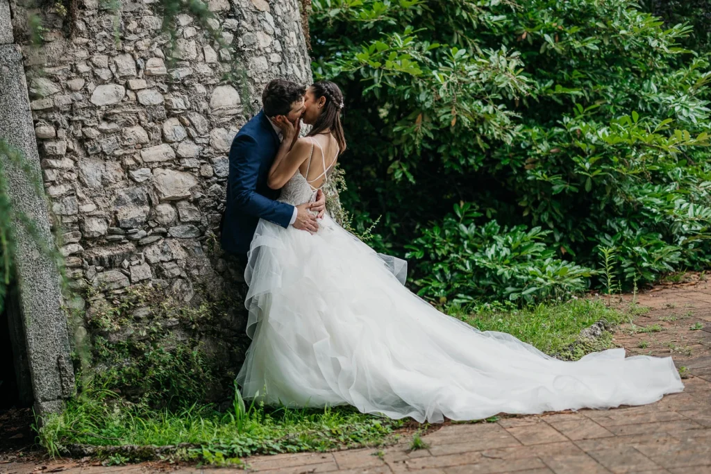 Dream Wedding at Villa Le Due Torrette in Erba: The Elegance of a Lake Como Celebration 53 Couple embracing by a stone wall in Villa Le Due Torrette gardens