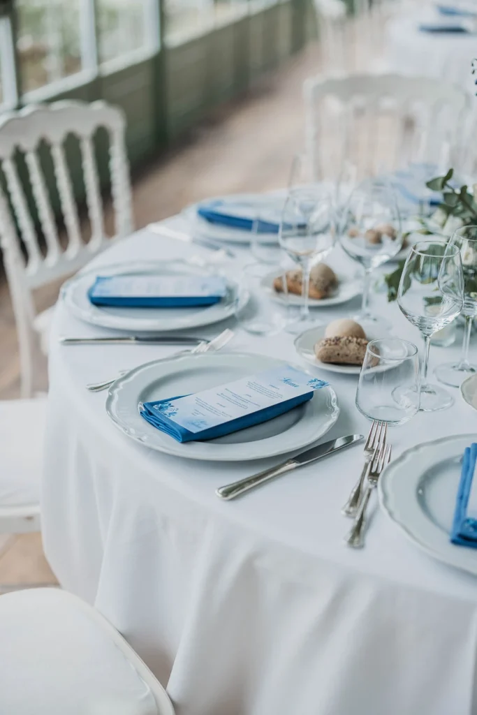 Dream Wedding at Villa Le Due Torrette in Erba: The Elegance of a Lake Como Celebration 67 Close-up of wedding table setting with blue napkins and crystal glasses