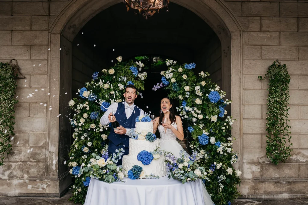 Dream Wedding at Villa Le Due Torrette in Erba: The Elegance of a Lake Como Celebration 81 Couple cutting wedding cake in front of floral backdrop at Lake Como villa