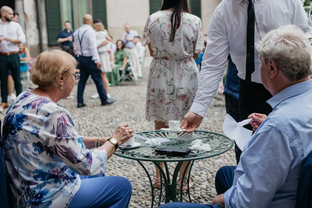 Dream Wedding at Villa Le Due Torrette in Erba: The Elegance of a Lake Como Celebration 85 Guests seated at wrought-iron table in garden at Villa Le Due Torrette