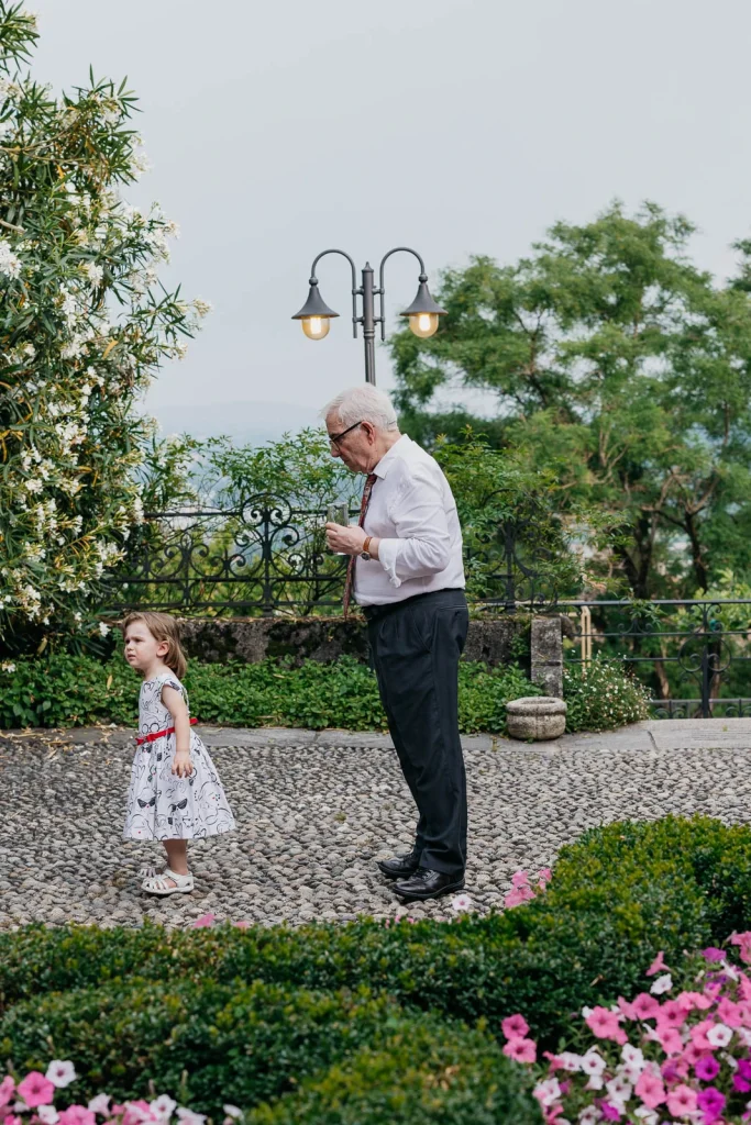 Dream Wedding at Villa Le Due Torrette in Erba: The Elegance of a Lake Como Celebration 87 Little girl walks alongside elderly guest in the garden of Villa Le Due Torrette