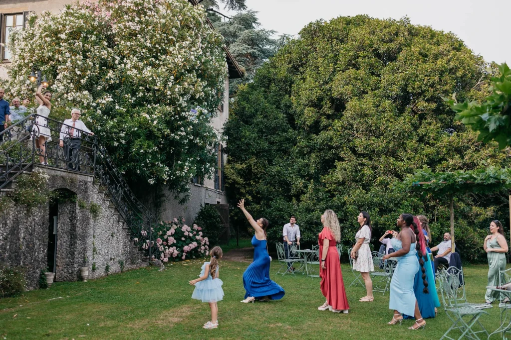 Dream Wedding at Villa Le Due Torrette in Erba: The Elegance of a Lake Como Celebration 89 Bride tossing bouquet in lush garden during Lake Como wedding with children