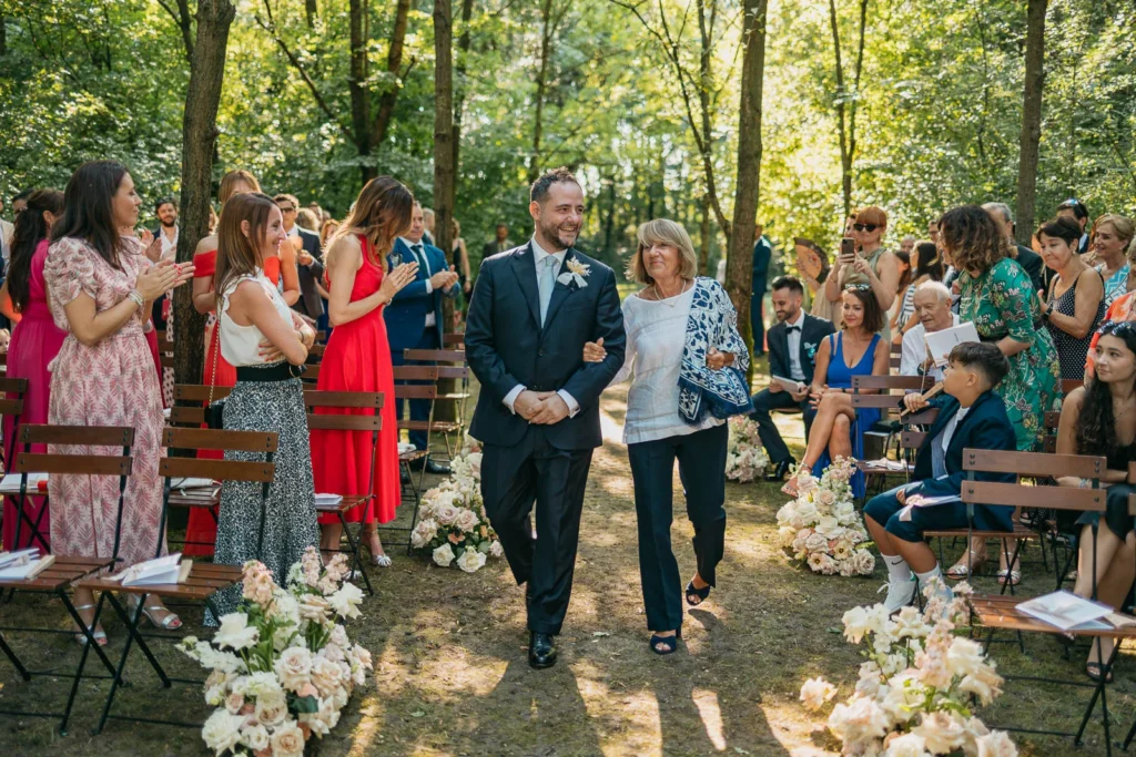 Groom walking down forest aisle among applauding guests