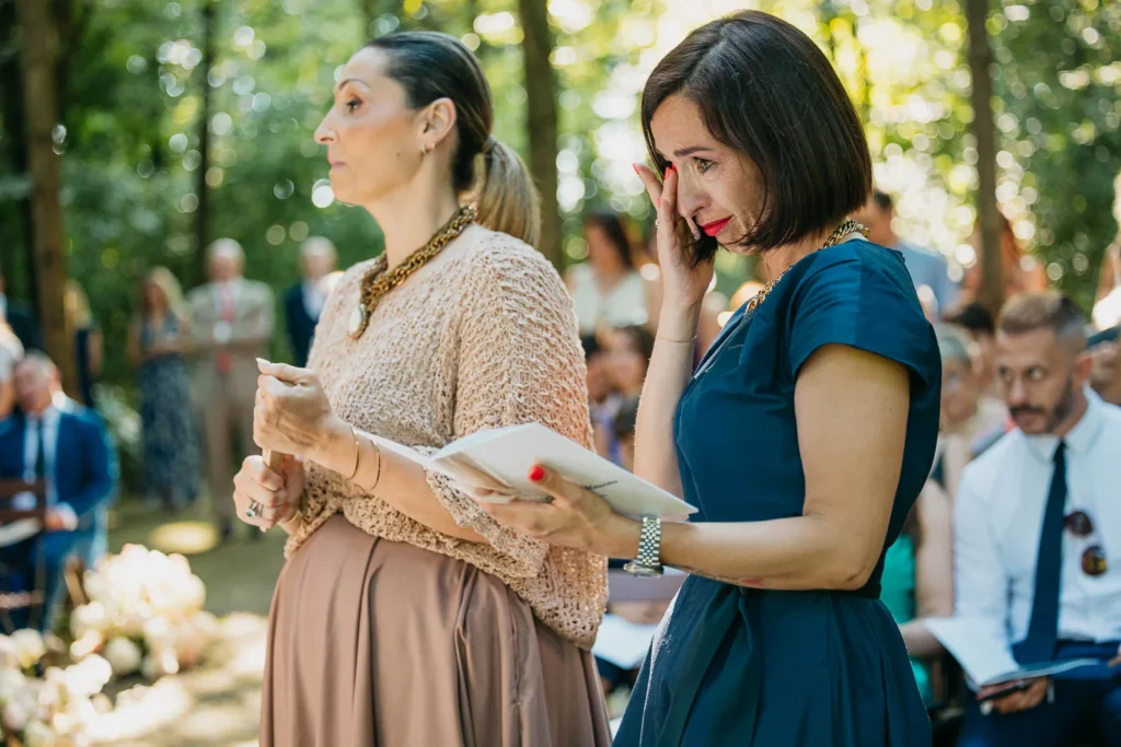 Guests reading wedding programs under the trees during the ceremony