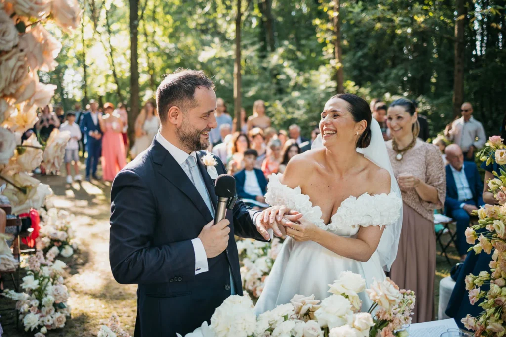 Groom holding bride’s hand while she reads her vows in the woods
