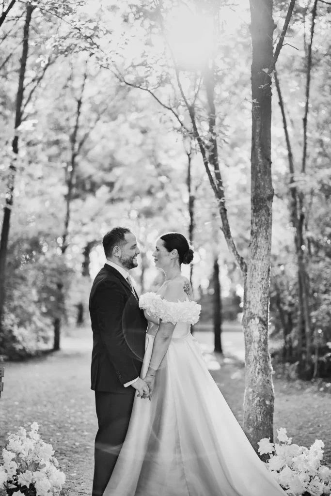 Black and white photo of bride and groom walking through woodland path