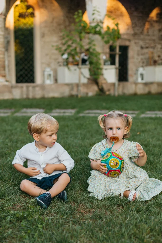 Two small children seated on grass during wedding reception in Italy