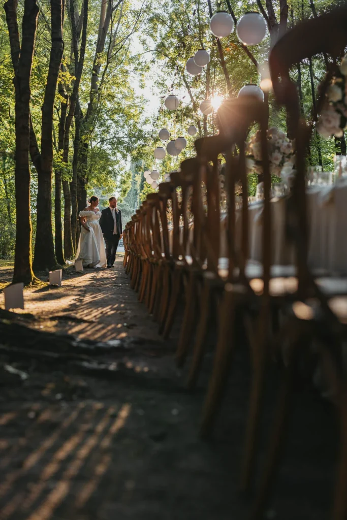 Newlyweds walking hand in hand under the trees toward the reception