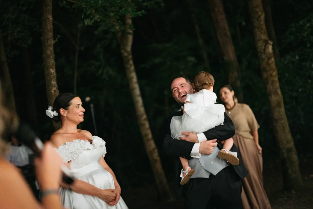 Bride smiling while holding her child at night in the forest