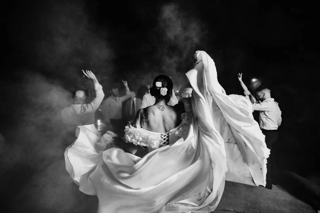 Artistic black and white shot of bride and guests dancing with veils flowing